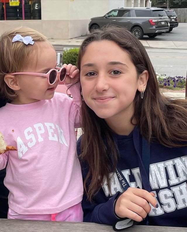 Kylie Rubin in a navy blue hoodie posing with her little sister in a pink t-shirt and shorts.